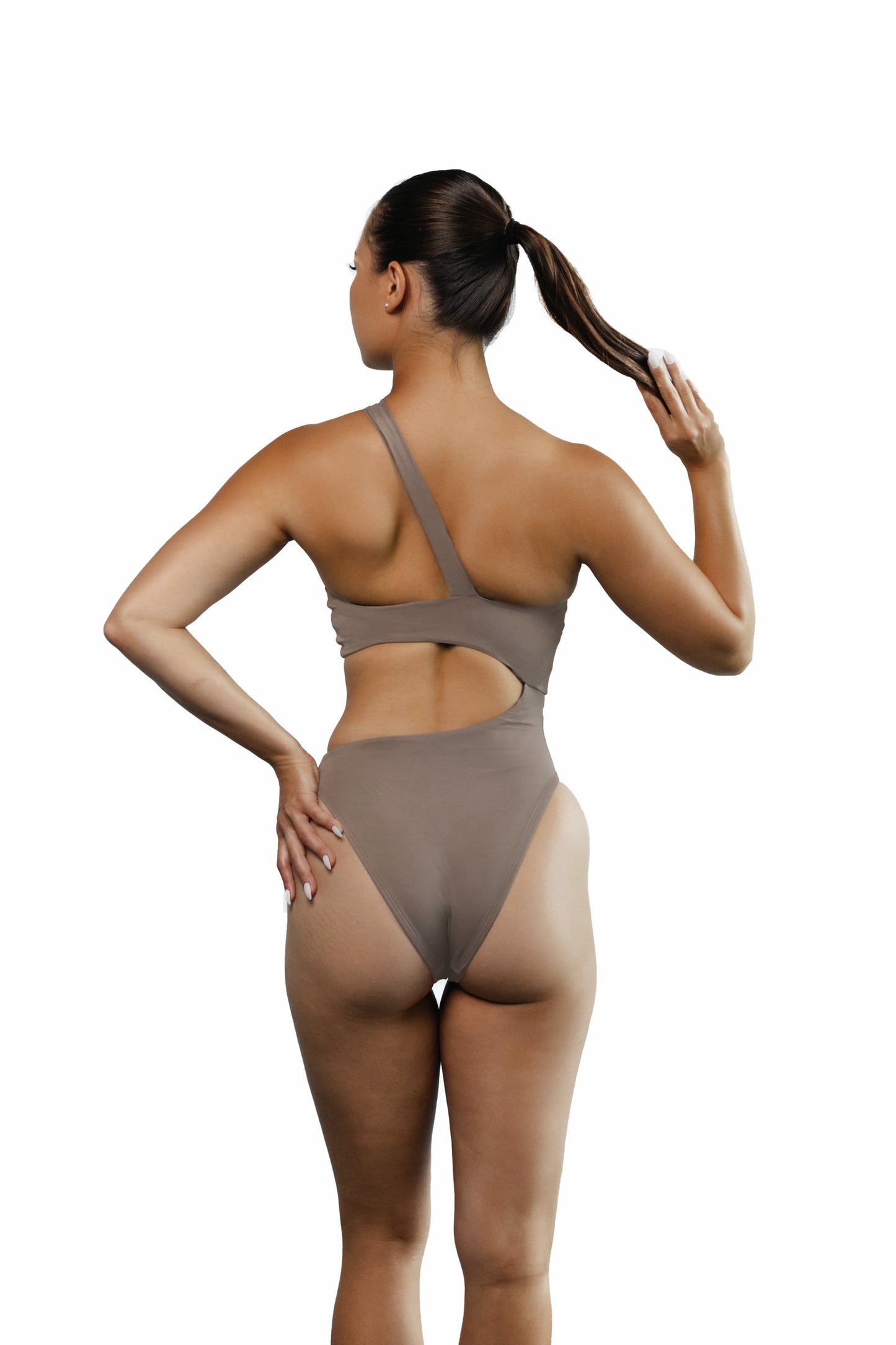 Model showing the back side of the Brooklyn one-piece cut-out swimsuit in Truffle color. Model is standing in front of white wall.